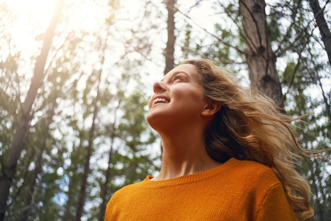 Een glimlachende jongevrouw geniet van het zonlicht in een bos