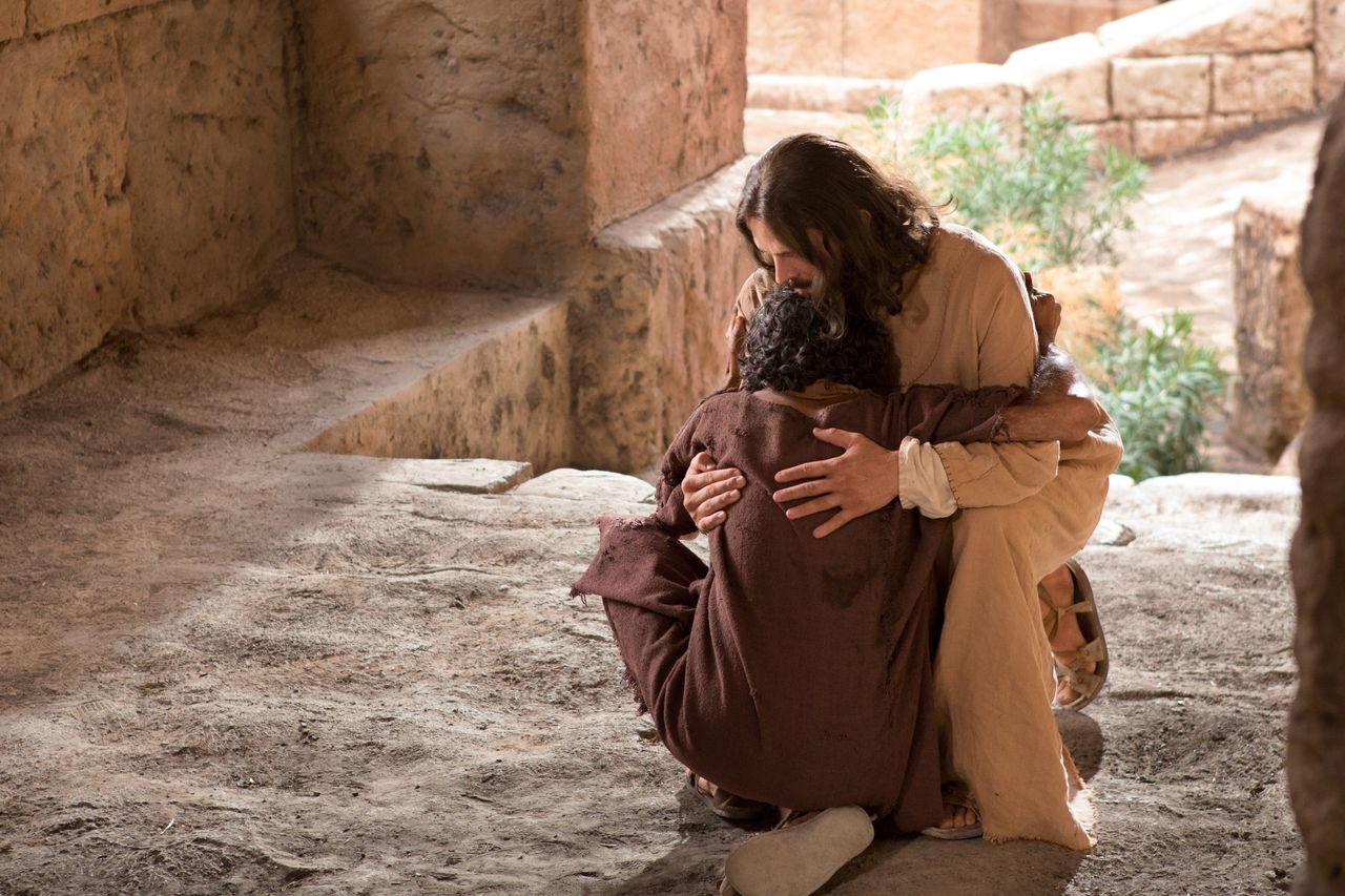 Man omhelst Jezus terwijl ze op de grond neerzakken