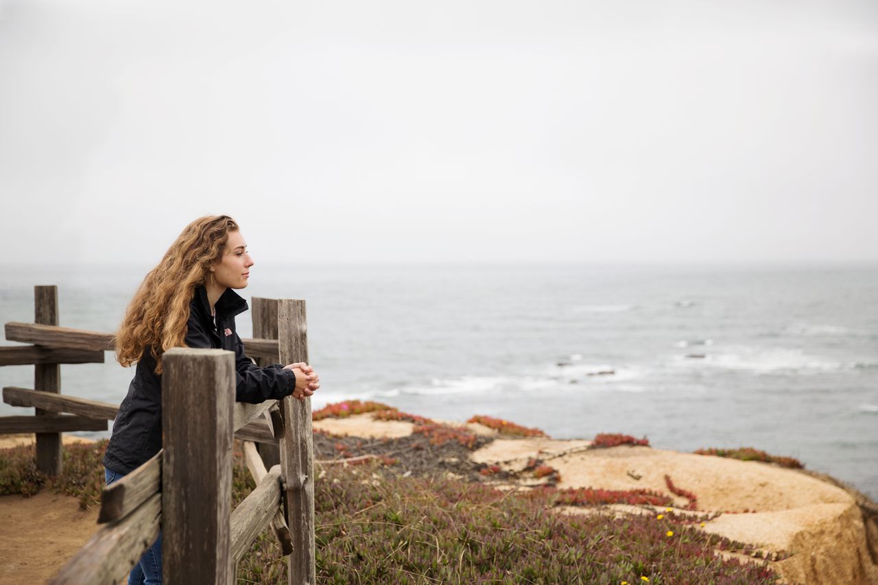 Een vrouw leunt op een reling aan de kust en overdenkt het evangelie van Jezus Christus